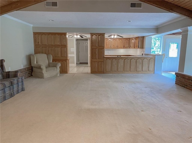 unfurnished living room featuring a textured ceiling, light colored carpet, crown molding, sink, and beamed ceiling