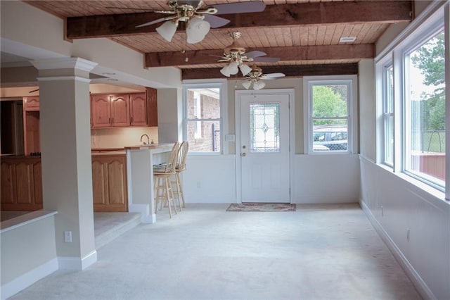 interior space featuring light carpet, ornate columns, wood ceiling, a breakfast bar, and beam ceiling