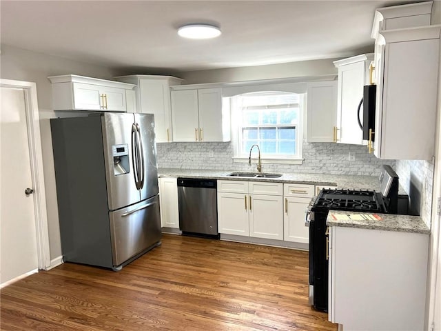 kitchen with hardwood / wood-style flooring, appliances with stainless steel finishes, light stone countertops, white cabinets, and sink