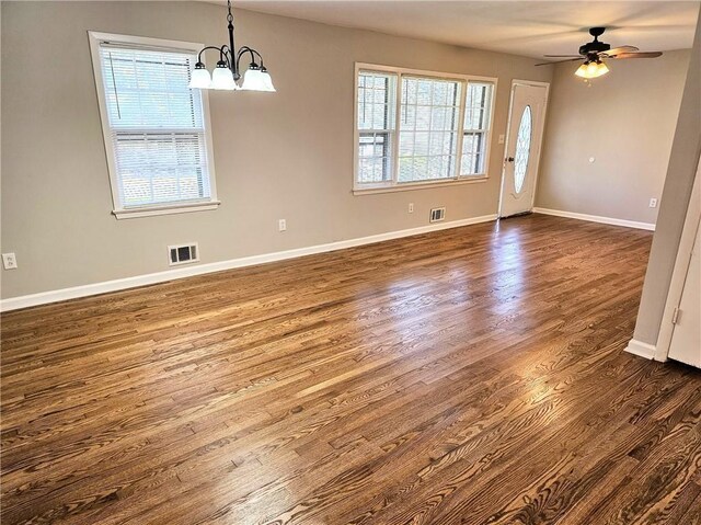 unfurnished dining area with dark wood-type flooring, a wealth of natural light, and ceiling fan with notable chandelier