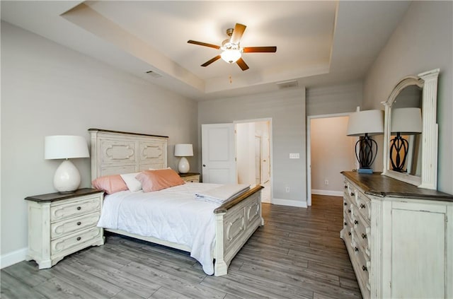 bedroom featuring ceiling fan, a raised ceiling, and light wood-type flooring