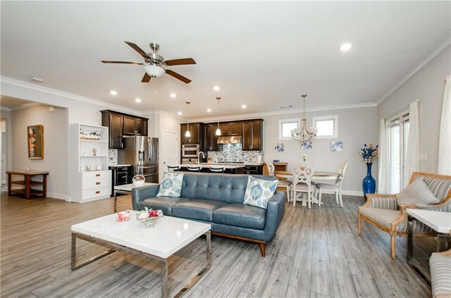 living room with ceiling fan with notable chandelier, light hardwood / wood-style floors, and crown molding