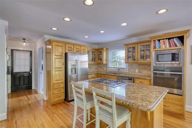 kitchen with appliances with stainless steel finishes, crown molding, a sink, backsplash, and light wood-style floors