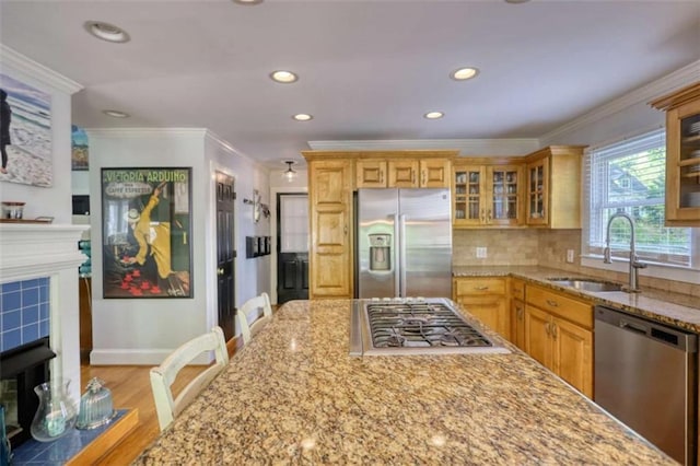 kitchen featuring stainless steel appliances, a sink, a tile fireplace, light stone counters, and baseboards