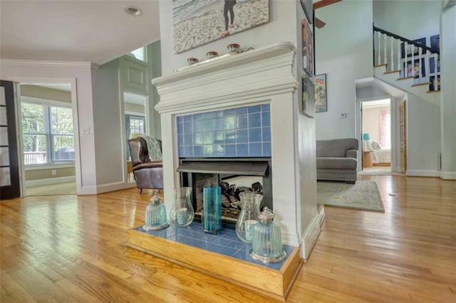 living room with baseboards, crown molding, wood finished floors, stairs, and a tile fireplace