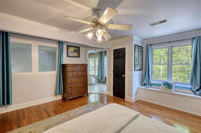 bedroom featuring light wood finished floors, crown molding, ceiling fan, and a wainscoted wall