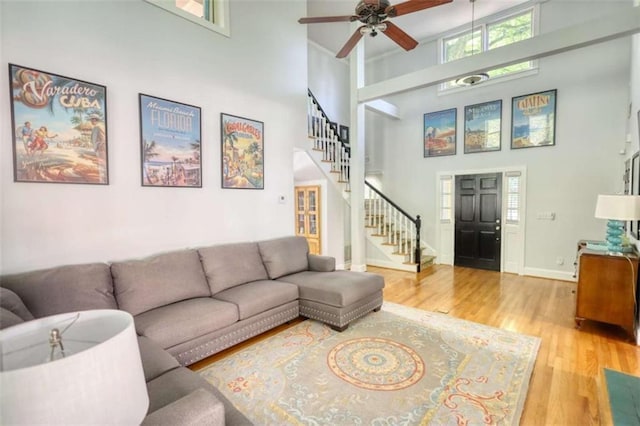 living room with stairway, a towering ceiling, wood finished floors, ceiling fan, and baseboards