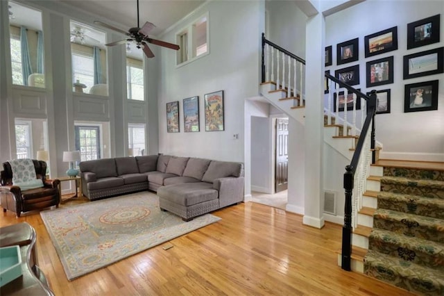 living area featuring a high ceiling, wood finished floors, stairs, a ceiling fan, and baseboards