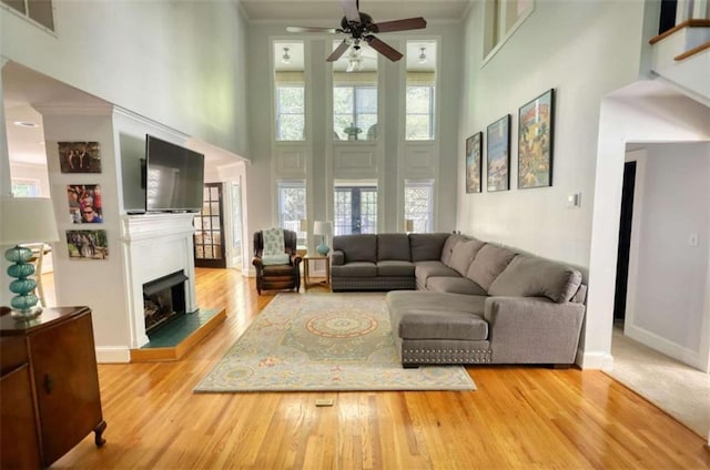 living area with a towering ceiling, a ceiling fan, wood finished floors, a fireplace with raised hearth, and baseboards