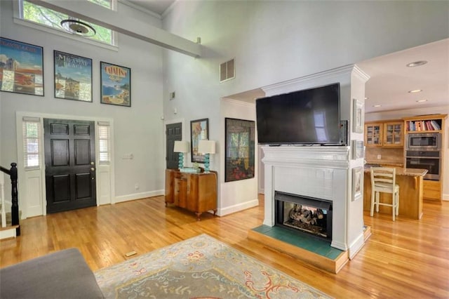 foyer entrance featuring a towering ceiling, light wood-type flooring, a tiled fireplace, baseboards, and recessed lighting