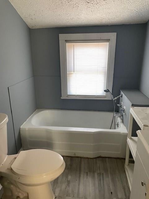 bathroom featuring vanity, hardwood / wood-style flooring, toilet, a tub to relax in, and a textured ceiling