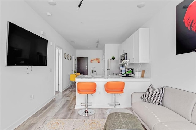 kitchen with kitchen peninsula, light hardwood / wood-style floors, a breakfast bar, white cabinetry, and appliances with stainless steel finishes