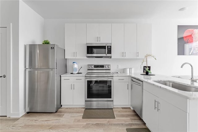 kitchen with kitchen peninsula, light hardwood / wood-style flooring, white cabinets, appliances with stainless steel finishes, and sink