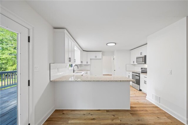 kitchen with kitchen peninsula, white cabinets, stainless steel appliances, light hardwood / wood-style floors, and light stone countertops