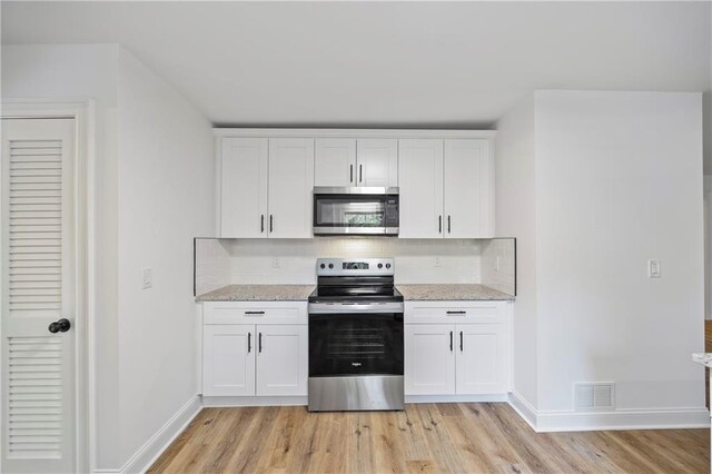 kitchen featuring appliances with stainless steel finishes, white cabinets, light wood-type flooring, and light stone countertops