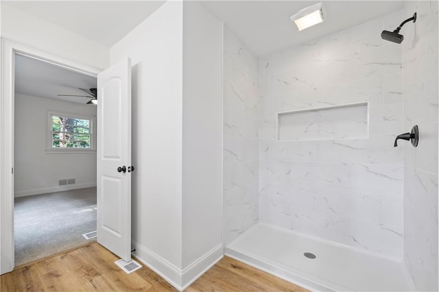 bathroom with tiled shower, wood-type flooring, and ceiling fan