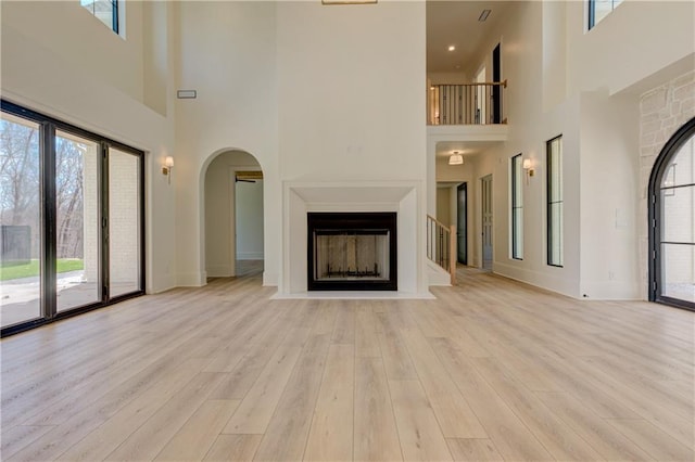 789 Old Mill Ct, Ball Ground, GA 30107 - unfurnished living room with a towering ceiling, plenty of natural light, light wood-style floors, a fireplace with flush hearth, and arched walkways