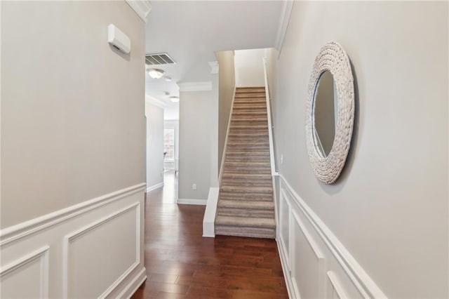 hallway featuring visible vents, dark wood finished floors, crown molding, a decorative wall, and stairs