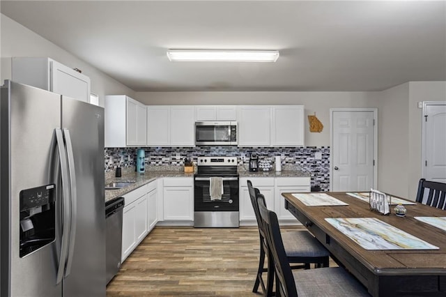 kitchen with stainless steel appliances, tasteful backsplash, light stone countertops, light hardwood / wood-style floors, and white cabinets