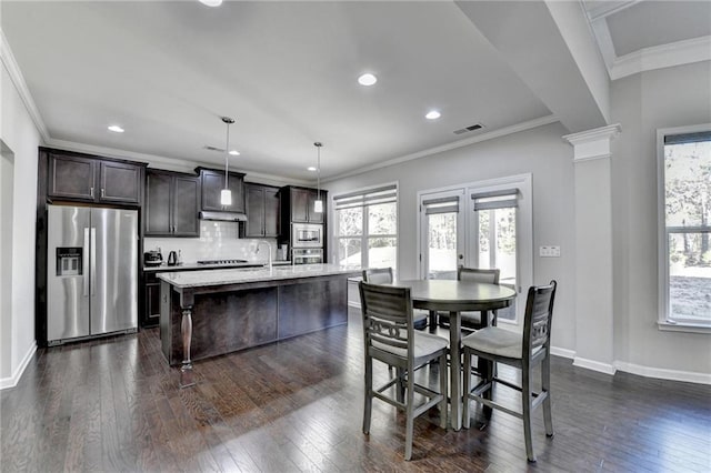 kitchen featuring backsplash, a kitchen island with sink, hanging light fixtures, appliances with stainless steel finishes, and a breakfast bar area