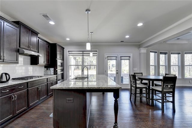 kitchen featuring light stone counters, sink, pendant lighting, stainless steel gas stovetop, and an island with sink