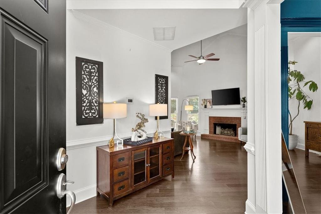 interior space with dark wood-style floors, a towering ceiling, a brick fireplace, ceiling fan, and baseboards