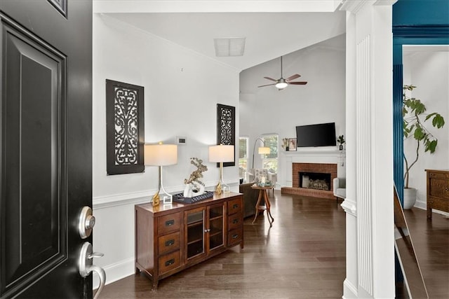 interior space with dark wood-style floors, a towering ceiling, a brick fireplace, ceiling fan, and baseboards