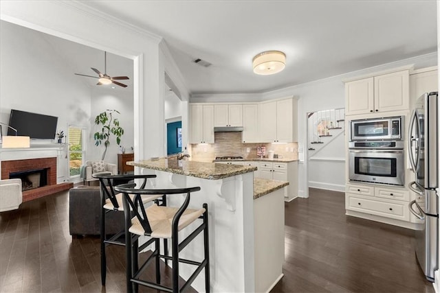 kitchen featuring light stone counters, a breakfast bar, open floor plan, stainless steel appliances, and under cabinet range hood