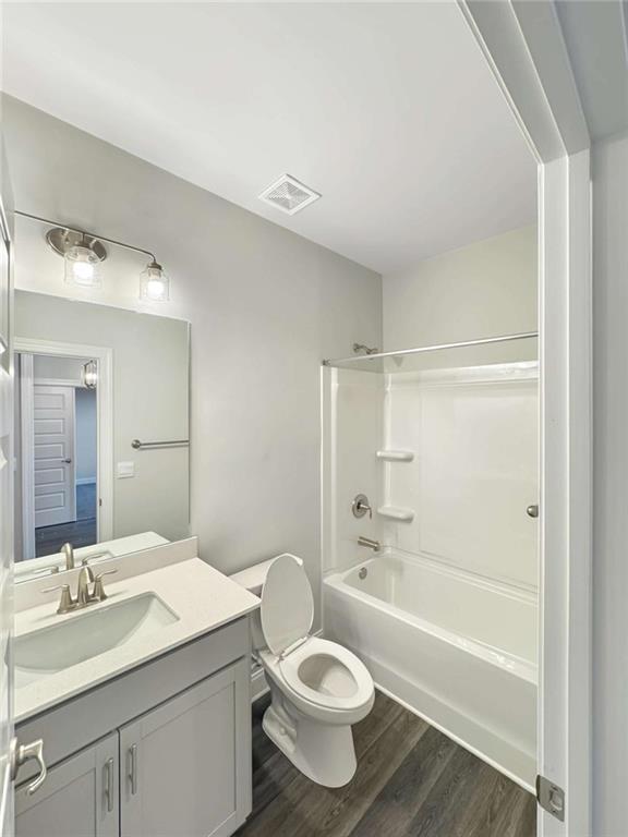 bathroom with visible vents, toilet, wood finished floors, vanity, and shower / bathing tub combination