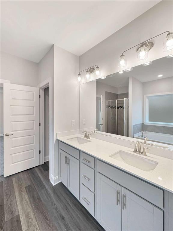 full bath featuring double vanity, a sink, a shower stall, and wood finished floors