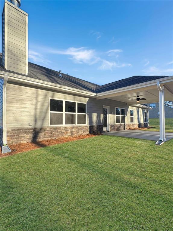 back of property with ceiling fan, stone siding, a lawn, and a chimney