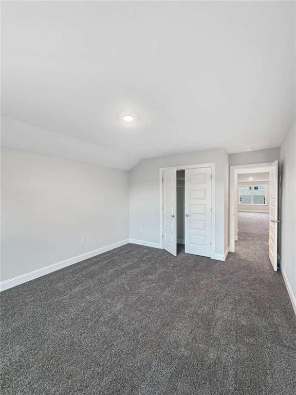 unfurnished bedroom featuring baseboards, dark carpet, vaulted ceiling, and a closet