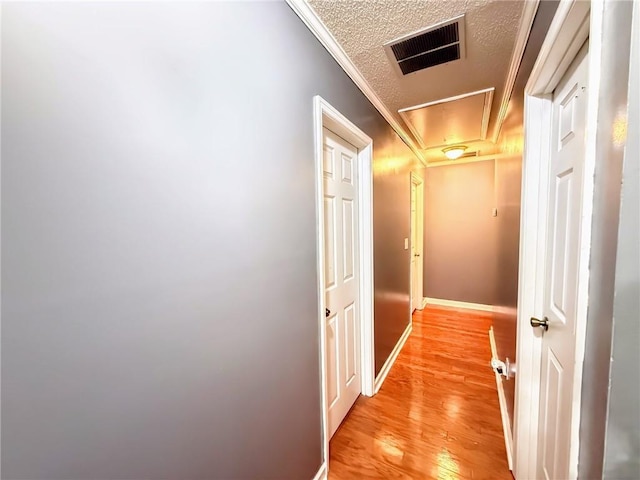 corridor with crown molding, a textured ceiling, and light hardwood / wood-style flooring