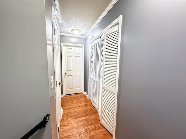 corridor featuring a textured ceiling, ornamental molding, and light wood-type flooring