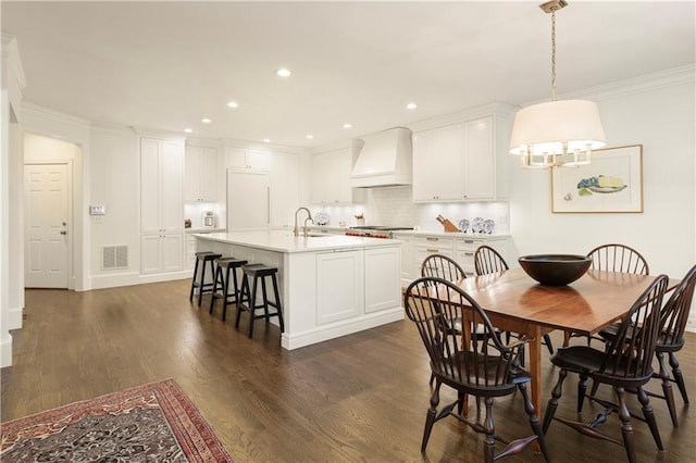 kitchen featuring a breakfast bar, dark wood-style flooring, a center island with sink, custom exhaust hood, and visible vents