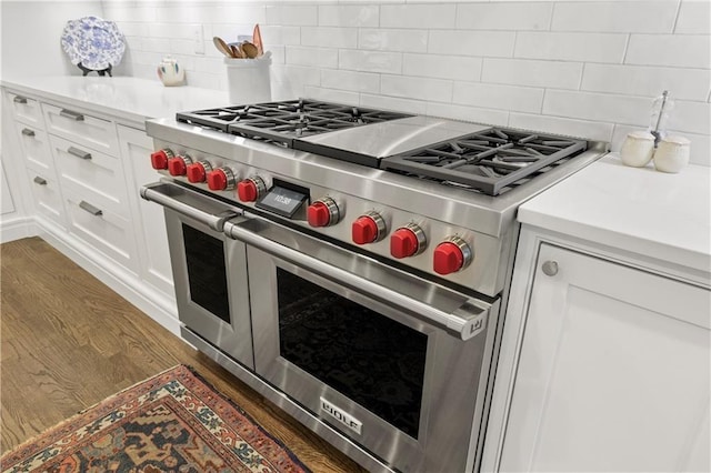 kitchen with wood finished floors, light countertops, double oven range, white cabinetry, and backsplash