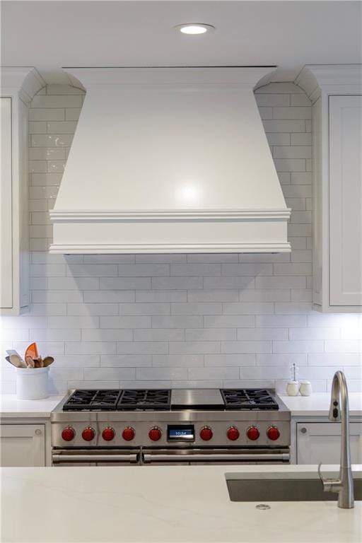 kitchen with range with two ovens, tasteful backsplash, custom range hood, white cabinets, and a sink