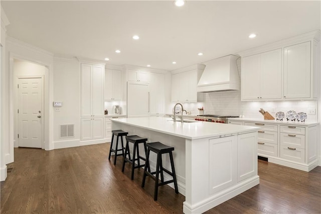 kitchen with visible vents, custom range hood, a kitchen island with sink, fridge, and a sink