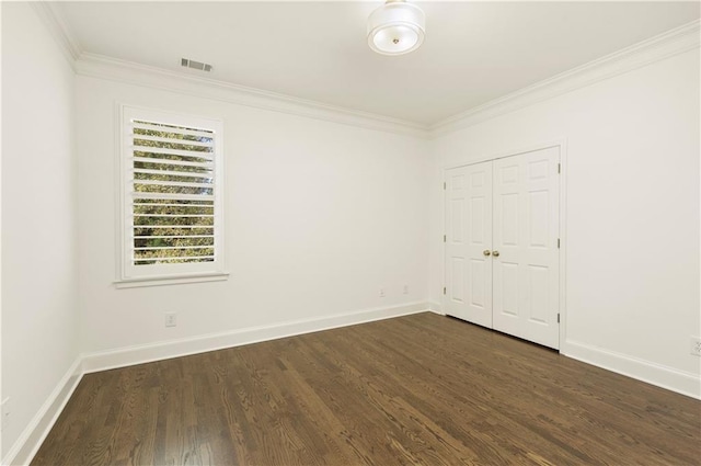 empty room featuring dark wood-type flooring, visible vents, crown molding, and baseboards