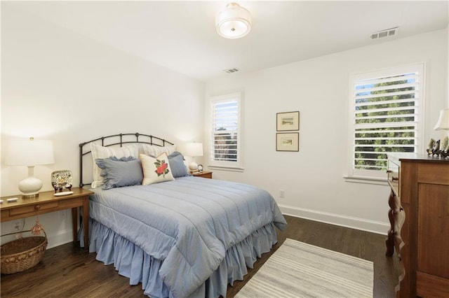 bedroom featuring baseboards, multiple windows, visible vents, and wood finished floors