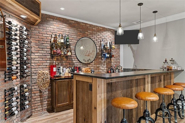 bar with brick wall, ornamental molding, light wood-type flooring, and indoor wet bar