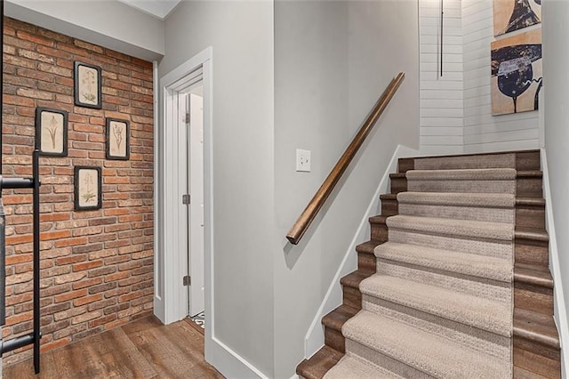 staircase featuring brick wall, baseboards, and wood finished floors