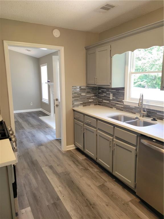 kitchen with backsplash, gray cabinetry, sink, dishwasher, and hardwood / wood-style floors