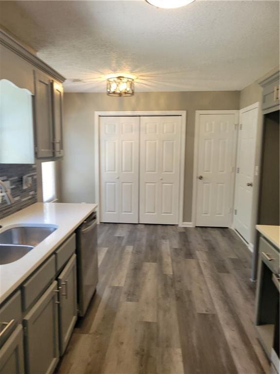 kitchen with gray cabinetry, sink, stainless steel dishwasher, dark hardwood / wood-style floors, and a textured ceiling