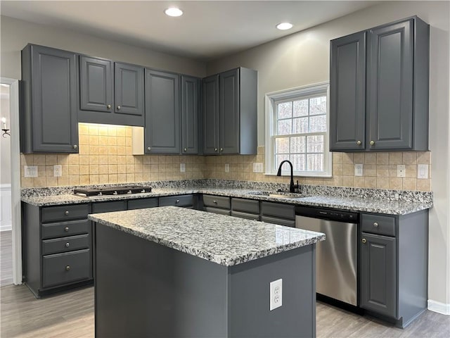 kitchen with sink, gray cabinets, appliances with stainless steel finishes, light stone counters, and a kitchen island