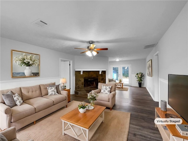 living room featuring ceiling fan, a fireplace, visible vents, and wood finished floors