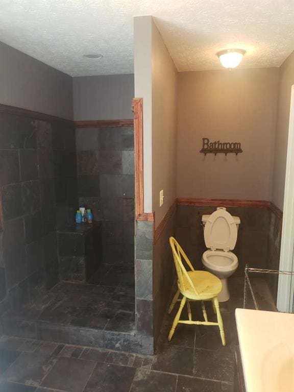 1383 Sims Rd, Winder, GA 30680 - bathroom with a textured ceiling, toilet, a tile shower, a wainscoted wall, and vanity