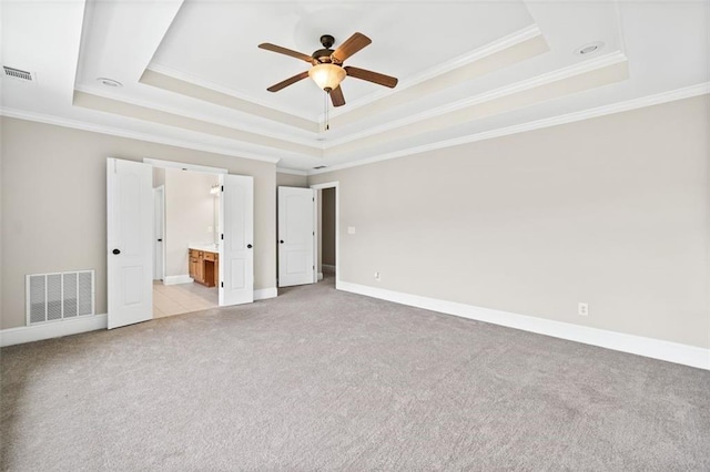 unfurnished bedroom with a tray ceiling, ceiling fan, ensuite bathroom, and crown molding