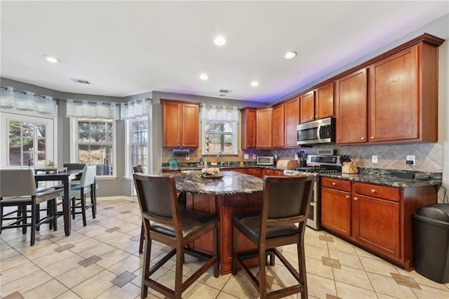 kitchen with appliances with stainless steel finishes, a breakfast bar, visible vents, and tasteful backsplash