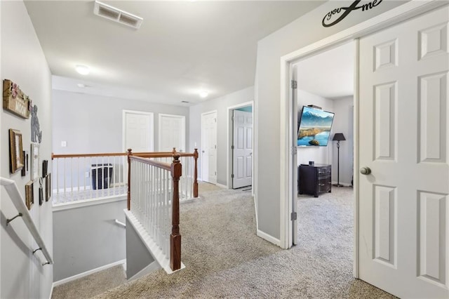 hallway featuring carpet, an upstairs landing, visible vents, and baseboards